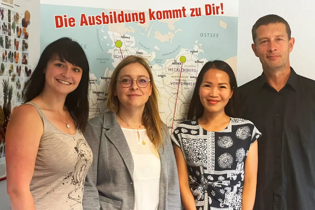 Team von torrivo und flycom - 3 Frauen und ein Mann, lächelnd vor torrivo-Plakat